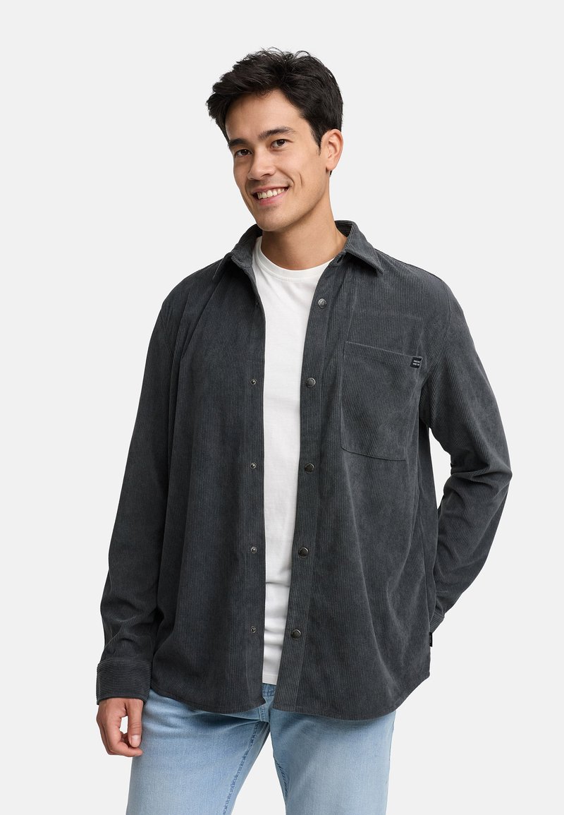 Grijze corduroy button-up shirt met een voorzak, gedragen over een wit T-shirt, gestyled met lichtblauwe jeans. Geweven stof met verticale strepen.