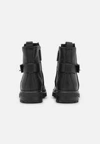 Botas de cuero negro hasta el tobillo con un acabado suave, que cuentan con un zipper trasero, una correa decorativa y una suela de goma resistente para ofrecer tracción.