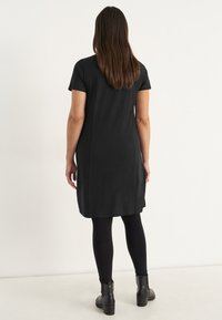Svart knälång klänning med korta ärmar, gjord av mjukt tyg. Bärs med svarta leggings och ankelstövlar. Enkelt mönster, utan mönster.