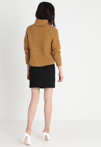 Hořčicový žebrovaný svetr s vysokým límcem, doplněný úzkou černou mini sukní a bílými vysokými podpatky. Měkká textura, volný střih.