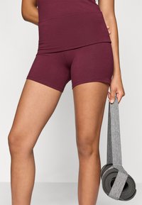 Μαρολαντζα αθλητικές βερμούδες από ελαστικό ύφασμα, στενή εφαρμογή, μήκος μέχρι το μέσο του μηρού, συνοδευόμενες από μια γκρι ζώνη γιόγκα που κρέμεται από το χέρι.