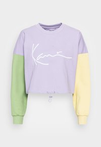 Sudadera recortada con cuerpo lila, manga izquierda verde, manga derecha amarilla, logo cursivo blanco en el pecho y cordón ajustable en el dobladillo.