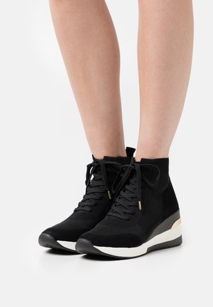 Sorte strikkede høj-top sneakers med en suedetå, snørebåndsdesign og hvid mellemsål, der er accentueret med en metallisk guldrand. Tekstur detaljer i stoffet.