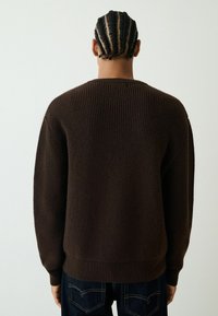 Dark brown ribbed knit sweater with a round neckline and relaxed fit, featuring a textured fabric and contrasting hem. Pairing with dark jeans.