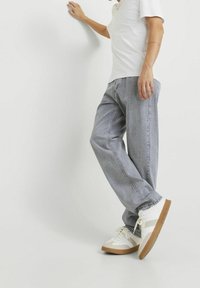 Jeans de mezclilla gris con un corte relajado, combinados con zapatillas blancas con acentos en marrón claro. El estilo es casual y versátil para el uso diario.