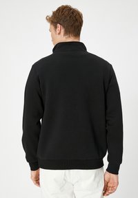 Svart sweatshirt med hög krage, ribbade ärmslut och nederkant. Tillverkad av mjukt tyg med slät textur, med en ren och minimalistisk design.