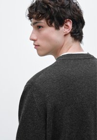 Tmavě šedý pletený svetr s kulatým výstřihem a texturovaným zakončením, zobrazený zezadu s kontrastními světlými límcem.