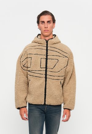 Man wearing beige fleece zip-up jacket with black abstract line design, standing against a plain white background.