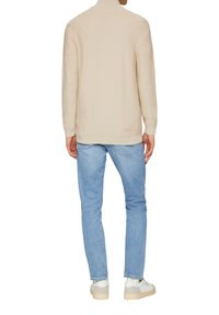 Beige strukturierter Pullover mit hohem Kragen, kombiniert mit hellblauen Jeans und weißen Sneakern. Lässiger Schnitt, klare Linien, keine sichtbaren Logos.