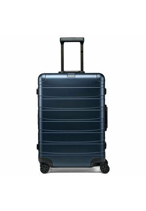 Maleta rígida azul marino con asa telescópica, cuatro ruedas giratorias y diseño horizontal acanalado.