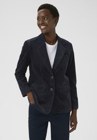 Dunkelblazer aus Cord mit Reverskragen, zwei vorderen Taschen und Zwei-Knopf-Verschluss. Aus einem strukturierten Stoff mit taillierter Passform.