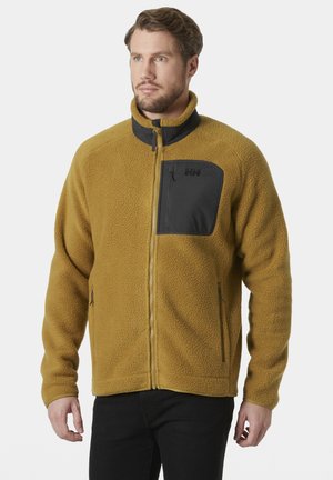 Fleece jack in mosterdgeel met zwarte accenten. Beschikt over een hoge kraag, een ritssluiting aan de voorkant en een borstzak. Textuurafwerking.