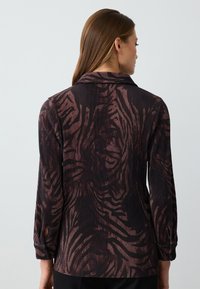 Blusa a maniche lunghe nera e bordeaux con pieghe verticali e una stampa animale testurizzata. Caratterizzata da un colletto a camicia e polsini con bottoni.