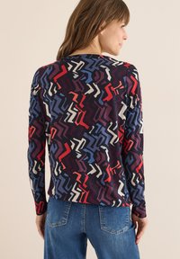 Langarmshirt mit einem mehrfarbigen abstrakten Muster in Rot, Blau und Weiß auf einem dunklen Hintergrund. Hergestellt aus weichem, dehnbarem Stoff.