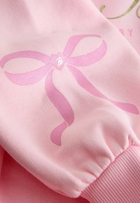 Rosa Sweatshirt mit einem glänzenden pinken Schleifengrafik-Design, das ein Herz und den Buchstaben "B" enthält. Mit gerippten Bündchen und einer weichen Stoffqualität.