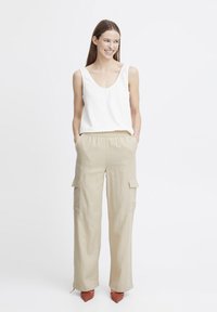 Top en lin blanc sans manches associé à un pantalon cargo beige à jambes larges, doté de poches latérales et d'une taille élastique, rehaussé de talons à motif corail.