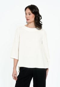 Maglietta bianca a maniche corte con scollo rotondo e silhouette rilassata, realizzata in un materiale morbido, abbinata a pantaloni neri.