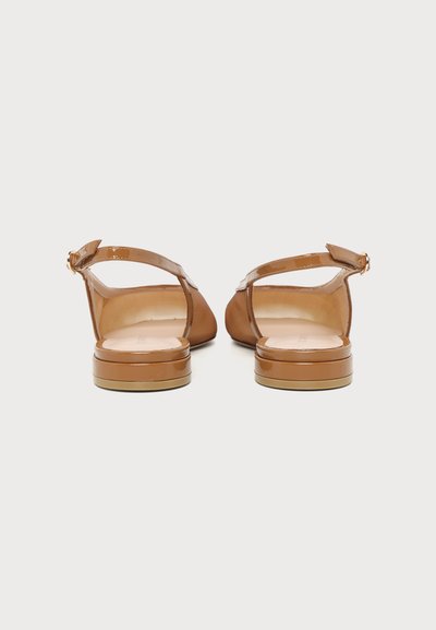 Pair of tan patent leather flat slingback shoes with ankle straps shown from the back on a plain light background.