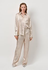 Metallic light gold silk shirt and matching trousers, featuring a button-up front, long sleeves, and a relaxed fit. Smooth texture with sheen.