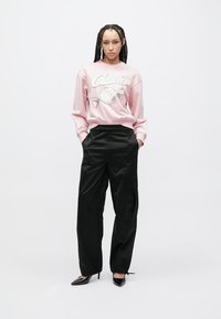 Ανοιχτό ροζ φούτερ με γραφικό τύπωμα, συνδυασμένο με μαύρο παντελόνι cargo. Το μοντέλο φοράει μαύρες μυτερές γόβες. Λείο ύφασμα, άνετη γραμμή.