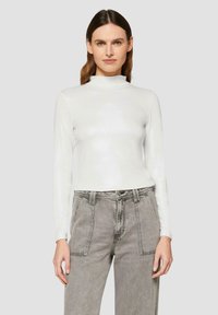 Weißes Langarmoberteil mit hohem Kragen, aus einem glänzenden Material, kombiniert mit grauen High-Waist-Jeans mit aufgesetzten Taschen.