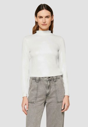 Witte langärmige top met hoge kraag, gemaakt van een glanzend materiaal, gecombineerd met hooggeplaatste grijze jeans met opgestikte zakken.