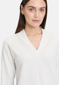 Pullover bianco testurizzato con scollatura a V e maniche lunghe, caratterizzato da un design a coste e una finitura liscia. Stile semplice e minimalista.