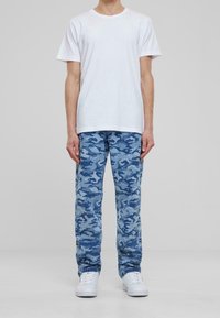 White short-sleeve t-shirt paired with blue camouflage patterned pants, featuring various shades of blue, textured fabric, and white sneakers.