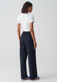 T-shirt blanc à manches courtes associé à un pantalon large bleu marine avec une taille élastique et des poches latérales, porté avec des sandales bleues.