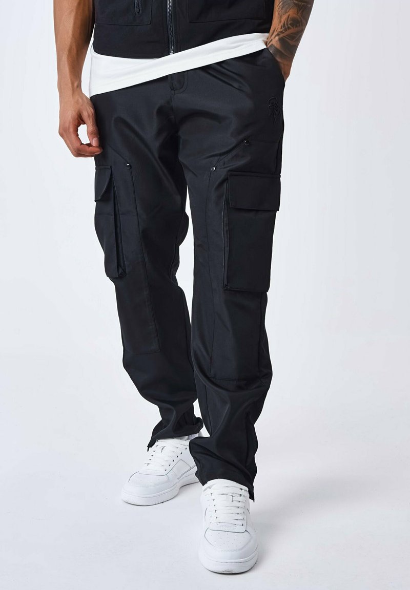 Sorte cargo-bukser med flere lommer, lavet af slidstærkt stof. Har en tapered fit og fremhævede sømme. Sammen med hvide sneakers.