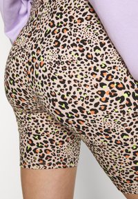 Shorts imprimé léopard en tissu doux et extensible, couleur beige avec des taches noires, orange et vertes. Longueur mi-cuisse avec coutures visibles.