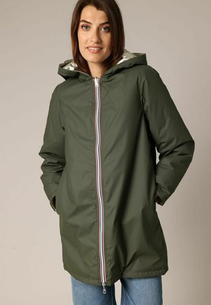 Veste imperméable vert olive avec capuche, doublure intérieure argentée, et fermeture éclair à l'avant ornée de bandes rouges, blanches et bleues.