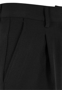 Pantalon noir avec un pli devant, une poche latérale et un détail passant de ceinture sur un tissu lisse.