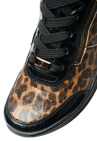 Close-up of a sneaker with black laces, leopard print leather, glossy black trim, and a gold zipper on the side.