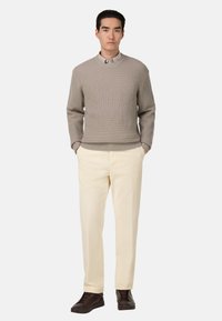 Svetle béžový žebrovaný pletený svetr spárovaný s krémovými kalhotami a tmavě hnědými sportovními botami. Tento outfit se vyznačuje hladkou texturou a uvolněným střihem.