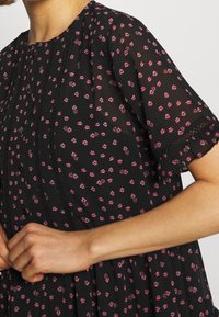 Czarna sukienka z różowym kwiatowym nadrukiem. Krótkie rękawy, zapinana z przodu na guziki z zakładkami oraz zdobiona koronką na krawędzi dołu i rękawów.