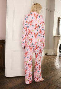 Rosa karierte Pyjamahose mit Hummer- und Sternmustern. Langärmliges Oberteil und lange Hose aus weichem Stoff, mit sichtbaren Steppnähten.