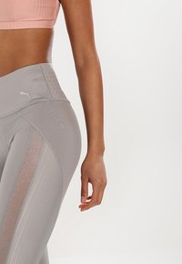 Leggings grigi alti in vita con una finitura texturizzata, dotati di pannelli in rete e di un logo discreto. Materiale morbido con design aderente.