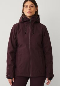 Bordeaux winterjas met rits aan de voorkant, verstelbare capuchon en twee zijzakken. Heeft elastische manchetten en een logo-detail op de mouw.