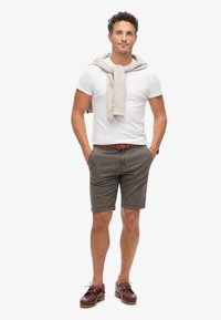 Conjunto masculino con una camiseta blanca, un suéter gris claro colgado sobre los hombros, pantalones cortos gris oscuro y zapatos marrones con cordones y un cinturón marrón claro.