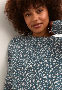 Chemise boutonée teal avec un motif abstrait blanc, texture douce, manches longues et encolure ronde avec un détail de patte.