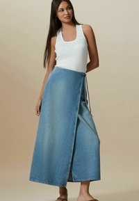 Lyseblå denim indpakningsskørt med snørelukning og en lang, flydende form. Sammen med en hvid tanktop med nagledetaljer.