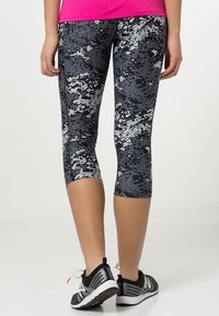 Leggings deportivas de patrón negro y gris con un diseño ajustado, largo por debajo de la rodilla y textura suave; combinados con zapatillas deportivas negras.