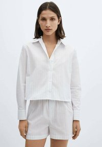 Vit randig kortärmad skjorta med lång ärm och knäppning, kombinerad med matchande shorts. Båda är gjorda av mjukt tyg med en lätt textur.