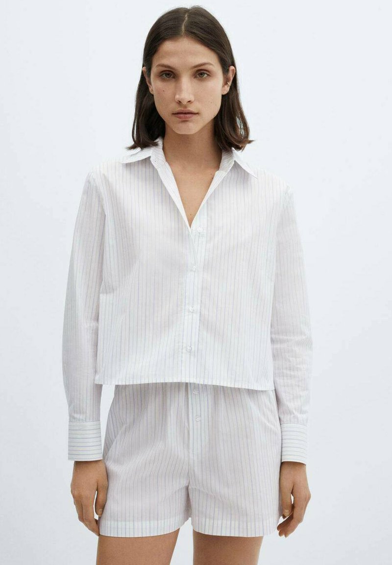 Vit randig kortärmad skjorta med lång ärm och knäppning, kombinerad med matchande shorts. Båda är gjorda av mjukt tyg med en lätt textur.