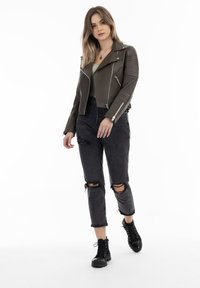 Oliven grøn læder bikerjakke med vandrette quiltede skuldre, parret med slidte sorte jeans. Modellen har sorte kampstøvler på.