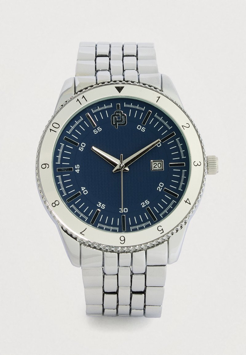 Ασημένιο μεταλλικό ρολόι με στρογγυλό μπλε καντράν με υφή, ασημένιους δείκτες ώρας και ένδειξη ημερομηνίας. Διαθέτει μπρασελέ από ανοξείδωτο ατσάλι.