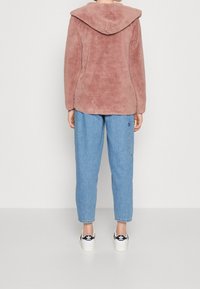 Fluffig rosa fleecejacka med en stor huva, med en mjuk textur. Kombinerad med ljusblå jeans och svarta och vita sneakers.