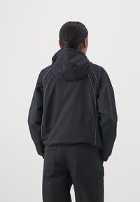 Svart huva jacka med avslappnad passform, med kontrasterande grå sömmar, elastiska ärmmuddar och dragsko vid huvan. Slät textur, lättviktig.