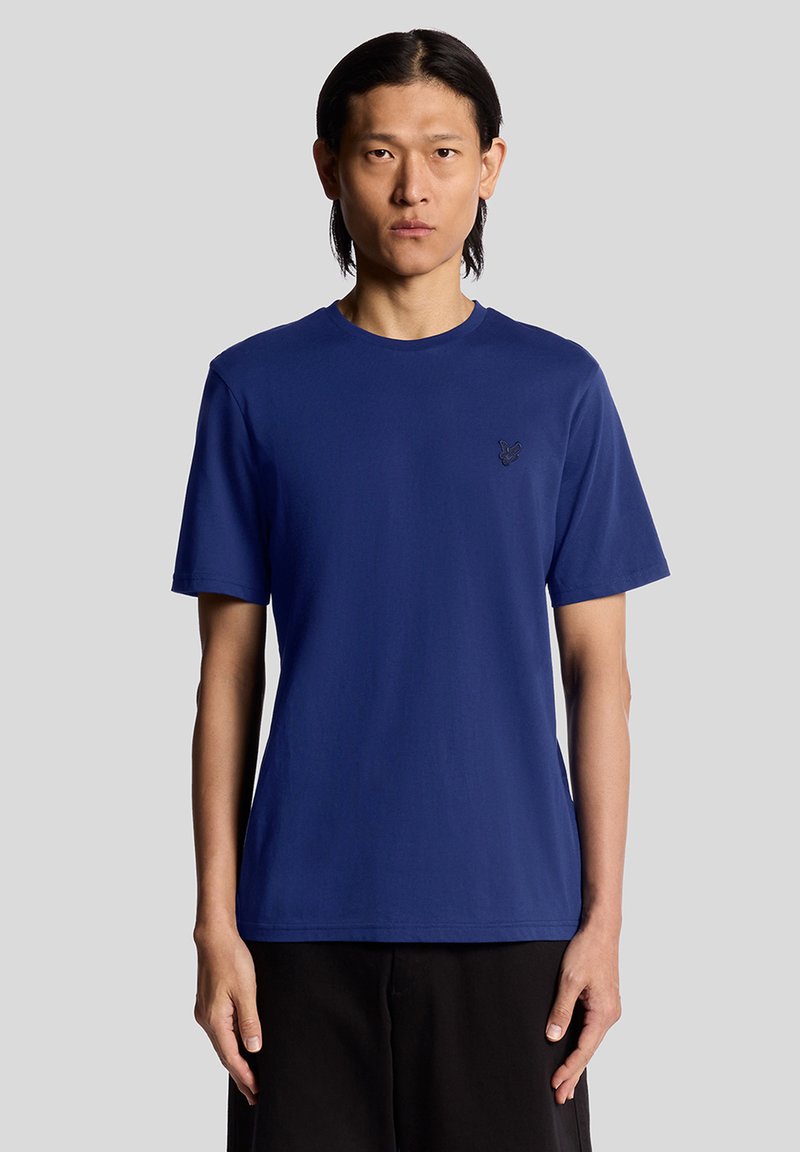 Marineblå t-skjorte laget av bomull med rund hals og korte ermer. Har en liten brodert logo på venstre bryst.